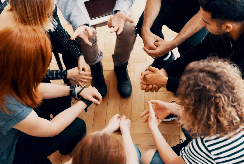 A high-angle view of a group of people sitting in a circle in a brightly lit room